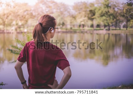 a young Asian woman wearing sport ware with pony tail hair putting her arm to waist prepare and ready for daily exercise activity, running or jogging, at the pond in the park in a summer morning day
