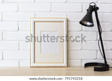 Gold decorated frame mockup with black table lamp near painted brick wall. Empty frame mock up for presentation artwork. Template framing for modern art.