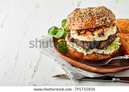 Hamburger in wholegrain bun with cheese, salad and walnuts, white wooden background