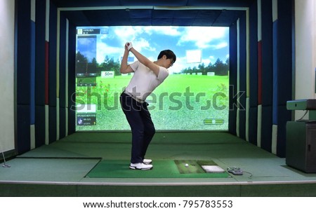 A  man enjoying screen golf with 7-iron backswing top motion, South Korea; Korean on the screen means information on swing and environmental condition  Royalty-Free Stock Photo #795783553