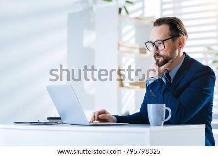 Working process. Thoughtful pleasant attractive man touching chin while using laptop and wearing glasses Royalty-Free Stock Photo #795798325