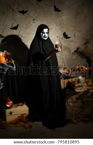 Mystic creature in black cloak holding candle in darkness