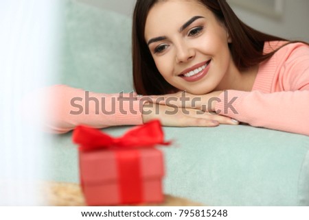 Beautiful young woman looking at gift box, closeup