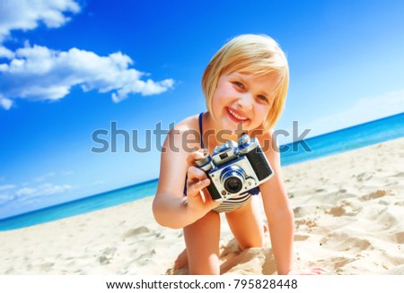 Sun kissed beauty. happy blond girl in beachwear on the seashore with digital camera taking photo