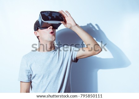 Young man wearing virtual reality goggles in modern coworking studio. Smartphone using with VR headset. Horizontal