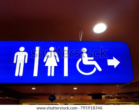 Sign with arrow pointing to the toilet for men, women and disabled on a blue background with white notation.