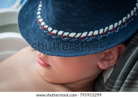 Young boy sleeping on the beach with his face covered with blue hat