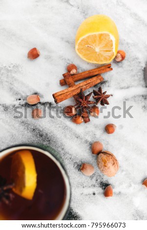 tea with lemon and cardamom in a green mug on a snowy background in the forest, top view, hazelnuts, cinnamon and cardamom