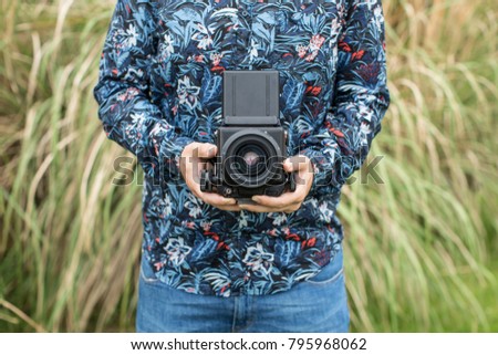 Crop unrecognizable man standing with film amera on background of grass.