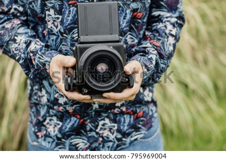 Crop unrecognizable man standing with film amera on background of grass.
