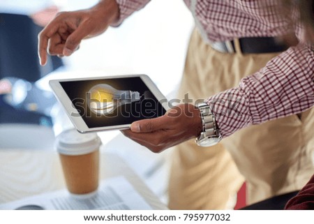 business, people and technology concept - close up of businessman with light bulb on tablet pc computer screen at office