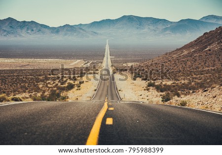 Classic panorama view of an endless straight road running through the barren scenery of the American Southwest with extreme heat haze on a beautiful sunny day with blue sky in summer Royalty-Free Stock Photo #795988399