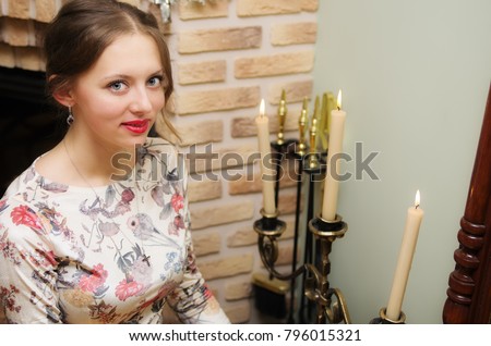 Girl posing in a beautiful dress sitting near a chandelier with candles / The picture was taken in the interior of a private house