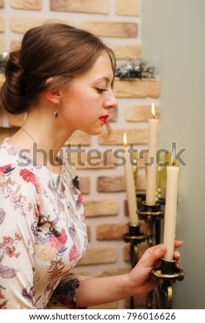 The girl in a beautiful dress corrects candle chandelier / The picture was taken in the interior of a private house