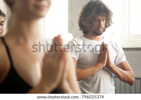 Group of young sporty people practicing yoga, making namaste gesture, closing eyes, hands together at the heart chakra, meditation, working out, indoor close up, studio. Wellness and wellbeing concept Royalty-Free Stock Photo #796025374