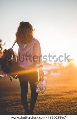 Woman standing carrying shoes at sunset