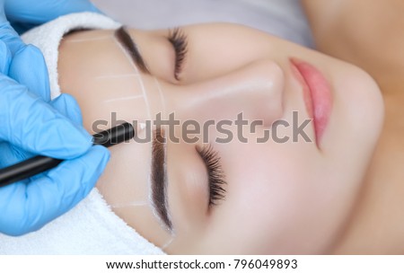 Permanent make-up for eyebrows of beautiful woman with thick brows in beauty salon. Closeup beautician doing  tattooing eyebrow. Royalty-Free Stock Photo #796049893