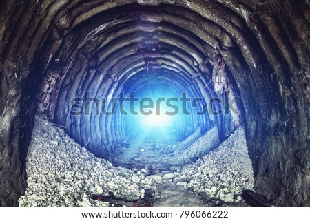 Mysterious blue light in the end of old round industrial tunnel or underground mine corridor. Escape and exit to freedom and hope concept, toned