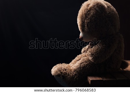 A lone Teddy bear sitting in the dark, side view, forgotten toy Royalty-Free Stock Photo #796068583