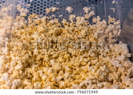 A closed up look through glass cabinet of salted butter popcorn in incubator machine at movie counter bar.