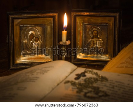 Icons of the Mother of God and Jesus Christ with a hymnal and a cross on a bonnet under the light of a candle Royalty-Free Stock Photo #796072363