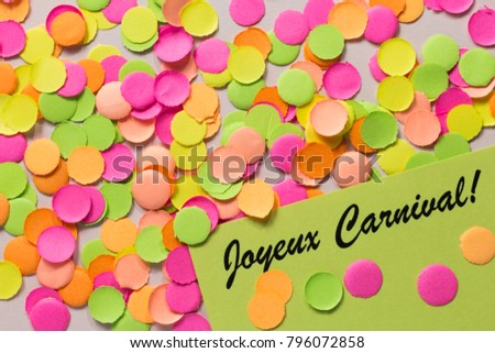 Brazilian Carnaval party background concept, space for text. Written the words in french: Joyeux Carnival. Colorful confetti spread over table. Warm colors: pink, yellow and orange.