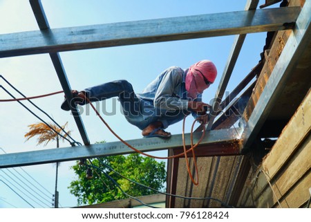 Welding steel worker. Renovation wooden house to new construction. Welds with argon-arc welding without mask for safety.