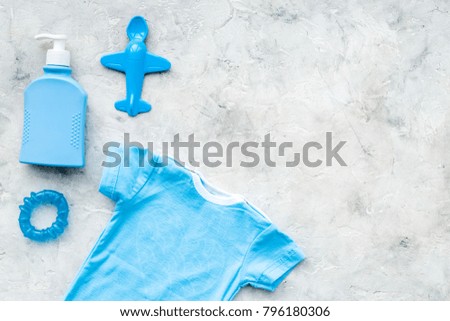 Blue baby clothes for little boy. Bodysuit, toys, cosmetics on grey background top view copy space