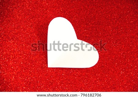 A white heart shape on a red glitter background.