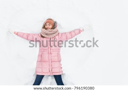 happy woman lying in the snow and moving arms and legs up and down, creating the shape of a snow angel. Smiling woman lying on snow in winter holiday ,for advertising ,background image
