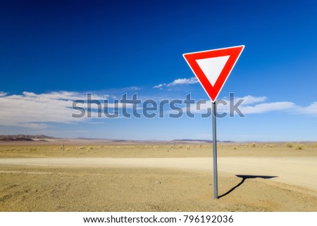 Wide angle view of a give way (yield) sign at a gravel road intersection in the Namibian Desert between Ai-Ais Fish River Canyon and Aussenkehr. Mountains in the background.