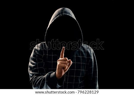 Silhouette of a man in a hood on a black background, his face is not visible, he lifts his finger up. The concept of a criminal, incognito, mystery, secrecy, anonymity. Royalty-Free Stock Photo #796228129