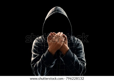 Silhouette of a man in a hood on a black background, his face is not visible, something that shows his hands. The concept of a criminal, incognito, mystery, secrecy, anonymity.