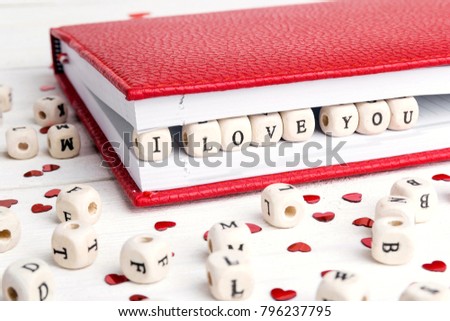 Love message written in wooden blocks  in a notebook  on white wooden table. Valentine's Day Concept. The inscription I love you.