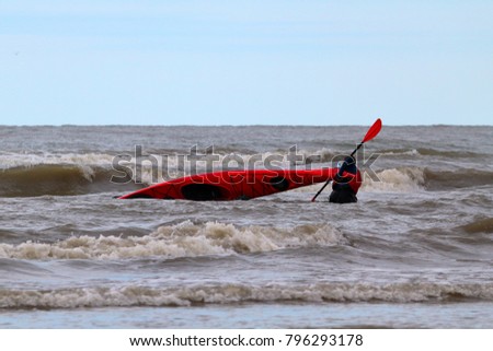 Man stands in Black sea surf wave an overturned red kayak