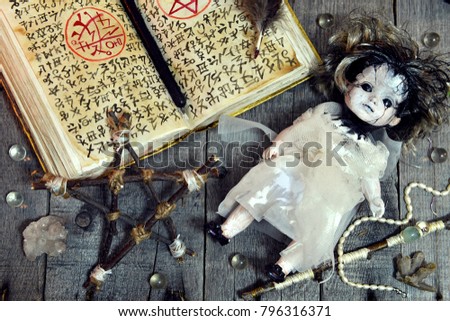 Scary doll, pentagram and open magic book with evil symbols on witch table. Occult, esoteric, divination and wicca concept. No foreign text, all symbols on pages are fantasy, imaginary ones