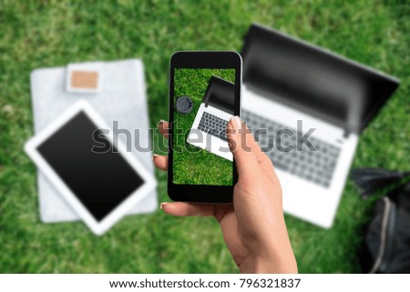 Female hand with a smartphone makes a photo laptop and coffee, outdoor office