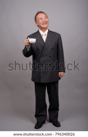 Studio shot of mature Asian businessman with coffee cup against gray background