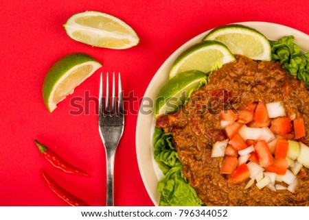 Spicy Mexican Style Beef Taco Meat and Salad With Fresh Limes Against A Red Background