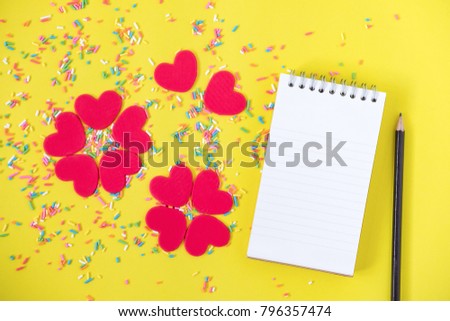 Red heart flower with colorful sprinkles, notebook and pencil on yellow background with copy space for your text. Concept for valentine's day celebration or couple of love.