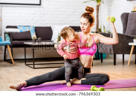 Portrait of a happy mother with her baby son exercising with dumbbells at home Royalty-Free Stock Photo #796369303