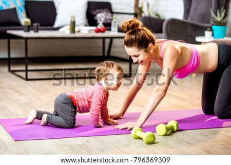 Young mother stretching on the mat with her baby son playing on the floor at home Royalty-Free Stock Photo #796369309