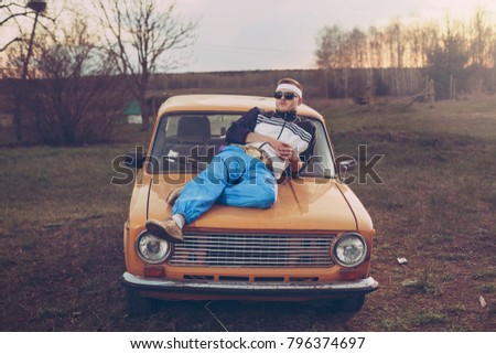 guy in the style of the 90s lies on the hood of an old car Royalty-Free Stock Photo #796374697