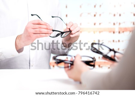Optician and customer choosing new glasses and trying different models. Eye doctor with client comparing spectacles and lenses in store.