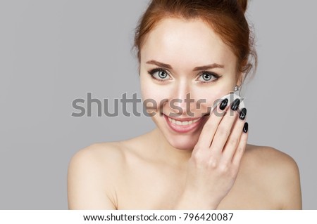 Portrait of cheerful laughing girl applying cotton wool and foam for washing on her face. Lovely woman redhead with attractive appearance. Skin Care spa relax concept on grey background