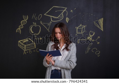 Serious girl looking into a notebook while standing next to a whiteboard with a picture of science and knowledge.