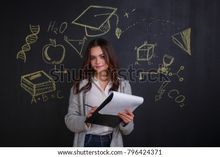 A young girl holding a black folder with papers, standing next to a whiteboard with a picture of sciences.