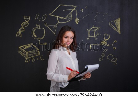 A girl looks and writes something in a folder with papers, standing next to a whiteboard.