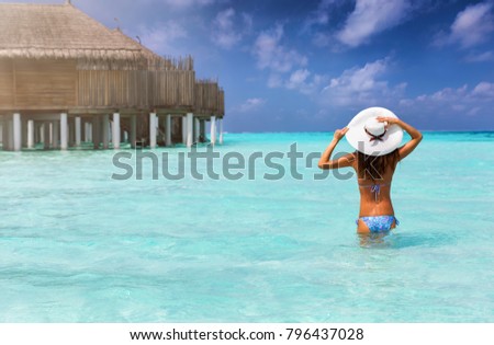 Traveller woman stands in tropical, turquoise waters and enjoys her vacation in the Maldives