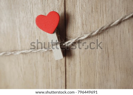 Red heart clip hanging on clothsline on wooden blackground.